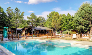Piscina y tumbonas rodeadas de árboles en Camping Luna del Monte, un parque vacacional en Umbría, Italia.