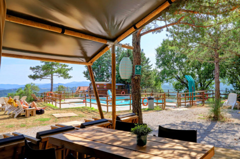 View from Camping Luna del Monte in Umbria, Italy, showing a pool, loungers, trees, and scenic mountain background.