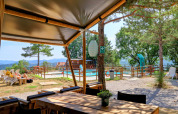 View from Camping Luna del Monte in Umbria, Italy, showing a pool, loungers, trees, and scenic mountain background.
