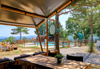 View from Camping Luna del Monte in Umbria, Italy, showing a pool, loungers, trees, and scenic mountain background.