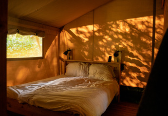 Interior de un dormitorio acogedor en una tienda safari en Camping de Zeven Heuveltjes, Países Bajos, con sol.