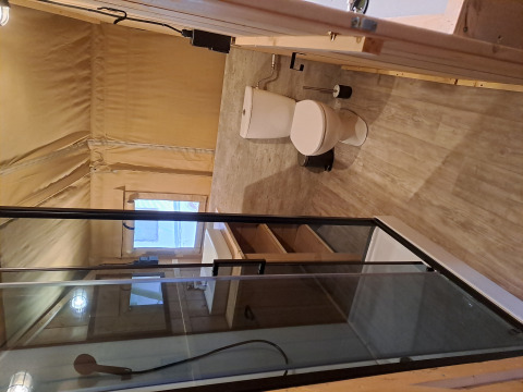 Interieur van een safaritent met moderne badkamer, glazen douche, toilet en houten vloer.