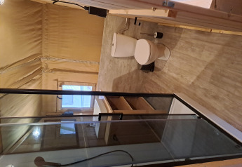 Innenansicht eines Safarizelts mit modernem Badezimmer, Dusche, Toilette und hellen Holzboden.