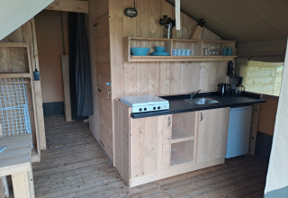 Área de cocina dentro de una tienda safari con estufa, fregadero y frigorífico en Camping de Zeven Heuveltjes.