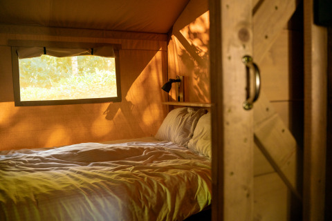 Interieur van een safaritent met bed en raam bij Camping de Zeven Heuveltjes in Nederland, zonlicht binnen.