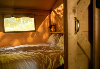 Interno di una tenda safari con letto e finestra al Camping de Zeven Heuveltjes, Paesi Bassi, illuminato dal sole.