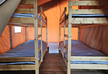 Vista interior de la tienda Safari en Camping Luna del Monte, Italia, con dos literas de madera.