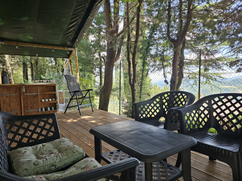 Terraza de tienda safari en Camping Luna del Monte, Italia, con sillas, mesa y vistas al bosque.