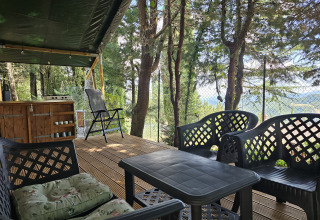 Veranda della tenda safari al Camping Luna del Monte in Italia, con sedie, tavolo e vista sul bosco.