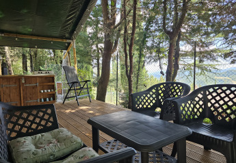 Deck of a safari tent at Camping Luna del Monte, Italy, with outdoor chairs, table, and forest view.