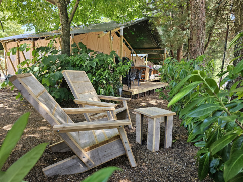 Safari-Zelt auf dem Campingplatz Luna del Monte in Italien, mit Holzstühlen unter Bäumen.