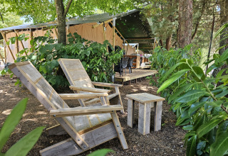 Tienda safari en Camping Luna del Monte, Italia, con sillas de madera rodeadas de vegetación.