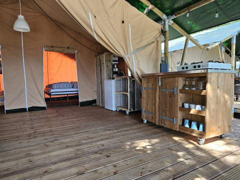 Indretning af safaritelte på Camping Luna del Monte i Italien med trægulv, køkken og seng.