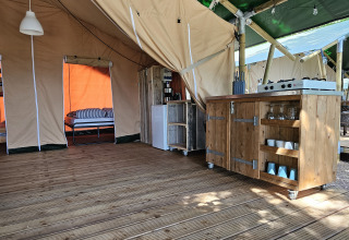 Interior de tienda safari en Camping Luna del Monte, Italia, con suelo de madera, cocina y cama.