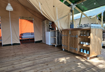 Interior de tienda safari en Camping Luna del Monte, Italia, con suelo de madera, cocina y cama.