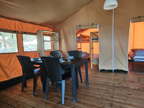 Interior de una tienda safari con mesa, sillas y literas en Camping Luna del Monte, Italia.
