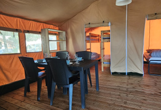 Interior de una tienda safari con mesa, sillas y literas en Camping Luna del Monte, Italia.