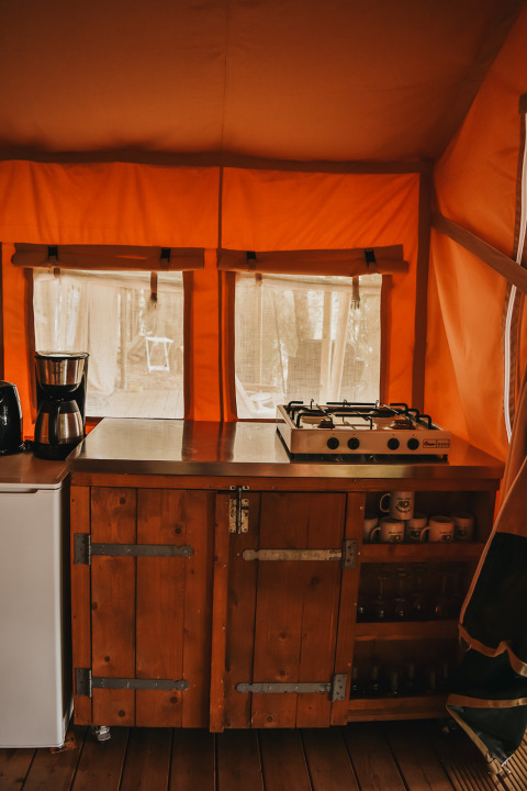 Zona de cocina con cafetera y cocina de gas en tienda safari en Camping Luna del Monte, Italia.