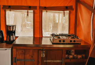 Zona de cocina con cafetera y cocina de gas en tienda safari en Camping Luna del Monte, Italia.