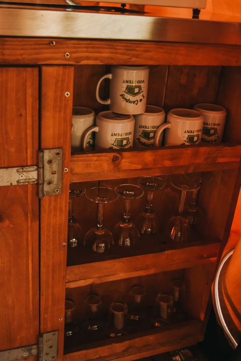 Ein Holzschrank mit Tassen, Weingläsern und kleinen Bechern im Safarizelt auf Camping Luna del Monte, Italien.