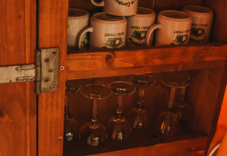 Un placard en bois avec des tasses, verres à vin et mugs dans une tente safari au Camping Luna del Monte, Italie.