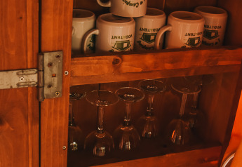 Un armario de madera con tazas, copas de vino y vasos dentro de una tienda safari en Camping Luna del Monte, Italia.