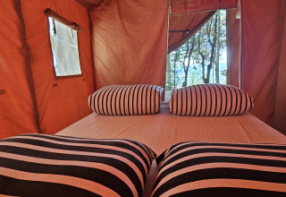 Interior de una tienda safari en Camping Luna del Monte, Italia, con almohadas a rayas y vista a los árboles.