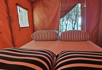 Interior de una tienda safari en Camping Luna del Monte, Italia, con almohadas a rayas y vista a los árboles.