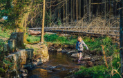 A child crosses a shallow stream beside the forest at Camping Braunlage holiday park, Lower Saxony, Germany.