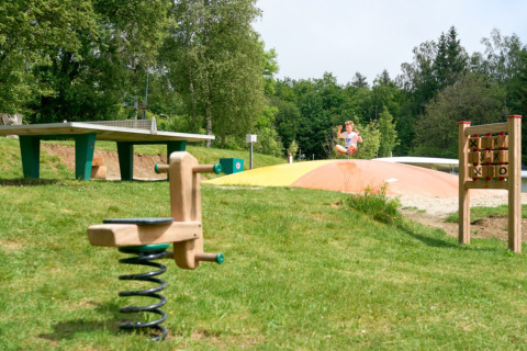 Spielplatz im Camping Braunlage, Niedersachsen, mit Hüpfkissen, Wippe und Tischtennisplatte im Grünen.