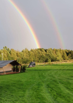 Doble arcoíris sobre campos verdes y tiendas en Camping de Regenboog, Ústí nad Labem, República Checa.