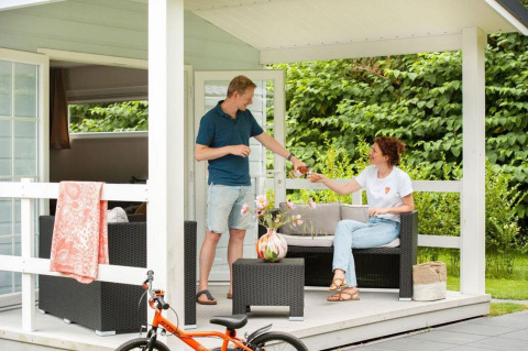 A couple enjoy drinks on the veranda of a chalet with hot tub at Camping Sevink Molen in the Netherlands.