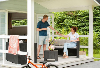 Et par nyder en drink på verandaen af ​​en chalet med spabad på Camping Sevink Molen i Holland.