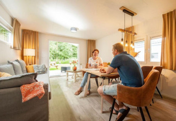 Et par sidder ved et bord i en hyggelig chalet med store vinduer og varm belysning, Camping Sevink Molen.