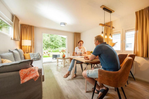 Koppel aan tafel in gezellig chaletinterieur bij Camping Sevink Molen, Nederland, met zicht op tuin.