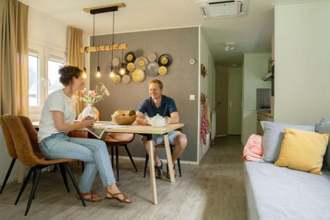 To personer sidder og nyder en samtale ved et spisebord i en moderne chalet på Camping Sevink Molen.