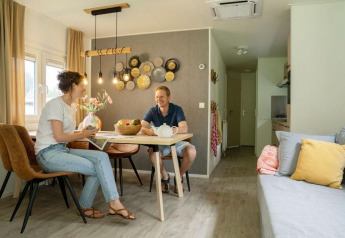 Twee mensen praten samen aan een eettafel in een sfeervol chalet bij Camping Sevink Molen in Nederland.