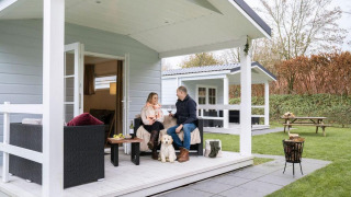 Coppia rilassata con il cane sulla veranda dello chalet presso Camping Sevink Molen, Paesi Bassi.
