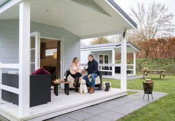 Coppia rilassata con il cane sulla veranda dello chalet presso Camping Sevink Molen, Paesi Bassi.