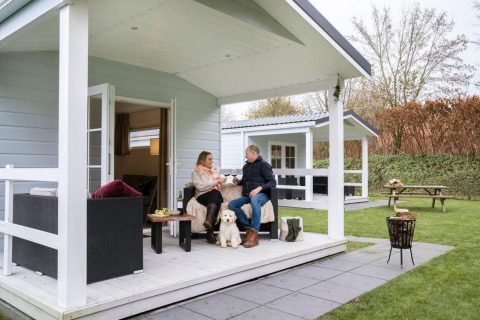 Couple se détendant avec un chien sur la véranda du chalet avec jacuzzi au Camping Sevink Molen, Pays-Bas.