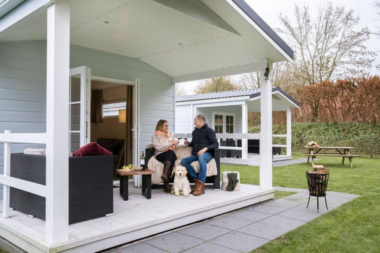 Paar entspannt mit Hund auf der Veranda des Chalets mit Whirlpool im Camping Sevink Molen, Niederlande.