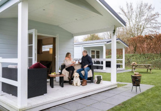 Pareja relajándose con perro en la terraza del Veranda chalet con jacuzzi en Camping Sevink Molen, Holanda.