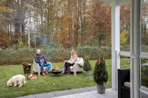 Coppia si gode il fuoco nel giardino del Veranda chalet al Camping Sevink Molen, Paesi Bassi, con cane.