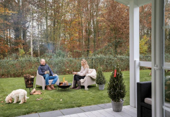 Pareja disfruta junto al fuego en el jardín del Veranda chalet en Camping Sevink Molen, Países Bajos, con perro.