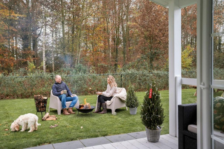 Paar genießt Feuer im Garten des Veranda Chalets bei Camping Sevink Molen, Niederlande, mit Hund.