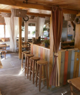 Hyggelig fælles spiseområde i Camping Lou Passavous med træmøbler og lyse gardiner i Provence.