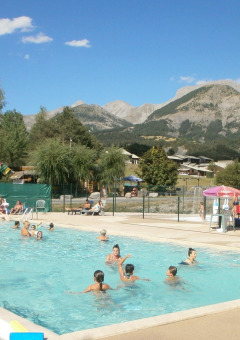 Piscina all'aperto al Camping Lou Passavous, persone che nuotano e vista sulle montagne delle Alpi.