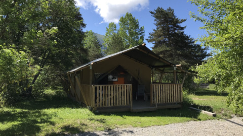 A cozy wooden and canvas cabin surrounded by green trees at Camping Lou Passavous in Provence-Alpes-Côte d’Azur, France.