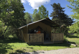 A cozy wooden and canvas cabin surrounded by green trees at Camping Lou Passavous in Provence-Alpes-Côte d’Azur, France.