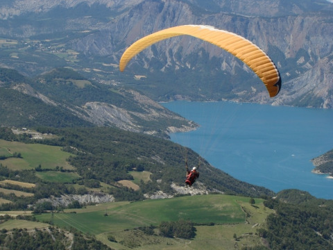 Parapente volando sobre campos verdes y un lago azul cerca de Le Vernet en Provenza-Alpes-Costa Azul, Francia.